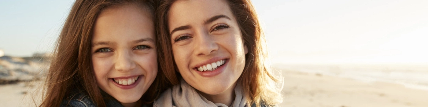 Deux femmes souriantes sur une plage regardant la caméra, lumière ensoleillée
